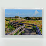 A boardwalk to the beach on a glossy greeting card