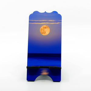 A photograph of a super moon over the ocean on a large phone stand with benelux top